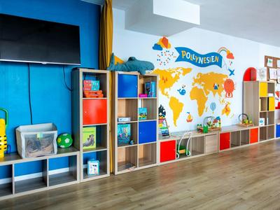 Pokój dziecięcy z kolorowymi półkami, telewizorem i mapą świata na ścianie.