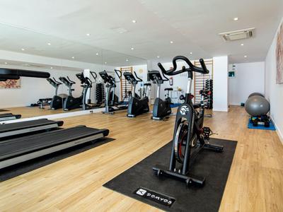 Salle de sport moderne avec tapis roulants, vélos et autres équipements sur sol en bois.