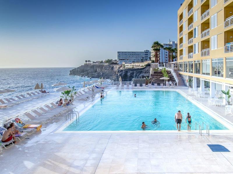 Basen hotelowy z widokiem na morze z gośćmi, otoczony słonecznym tarasem.