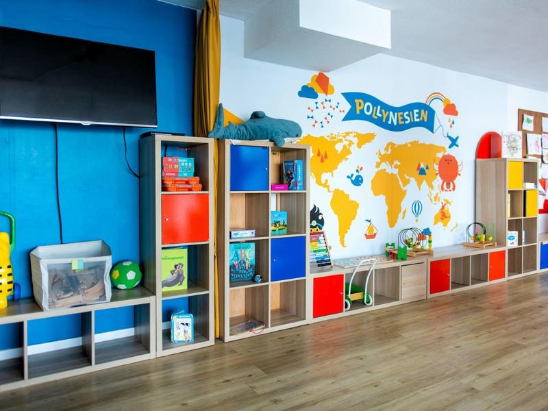 Pokój dziecięcy z kolorowymi półkami, telewizorem i mapą świata na ścianie.