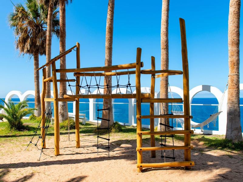 Plac zabaw na plaży z palmami i widokiem na morze w słoneczny dzień.