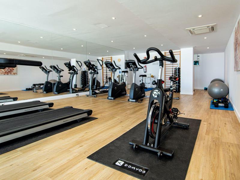 Jasno oświetlona siłownia z bieżniami, rowerami stacjonarnymi i lustrem.