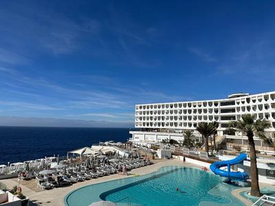 Moderner Hotelkomplex am Meer mit Outdoor-Pool, Wasserrutsche und Liegestühlen unter blauem Himmel.