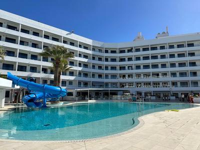 Großes Hotel mit mehrstöckigem Balkon, Pool mit Wasserrutsche und Palmen bei klarem Himmel.
