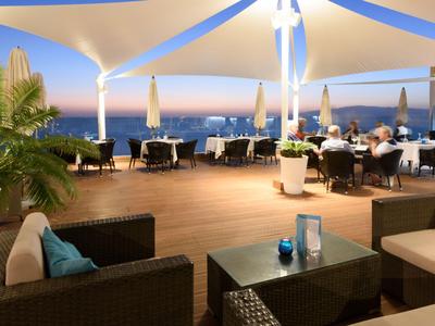 Offener Terrassenbereich mit Tischen, Stühlen und Blick auf das Meer bei Sonnenuntergang.