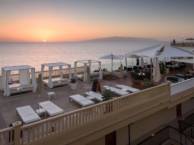 Sonnenuntergang über dem Meer mit Liegestühlen und weißen Strandkabinen an einem Hotelstrand.