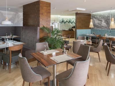 Modernes Restaurant mit Holztischen, grauen Stühlen und ansprechendem Interieur für Hotelgäste.