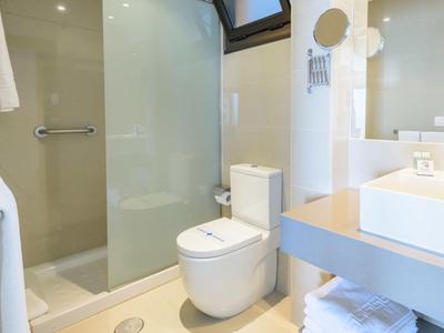 Helles Hotelbadezimmer mit Glasdusche, WC und Waschbecken mit Spiegel.
