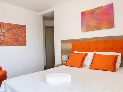 Modernes Hotelzimmer mit weißem Bett, orangen Akzenten und Wandkunst.