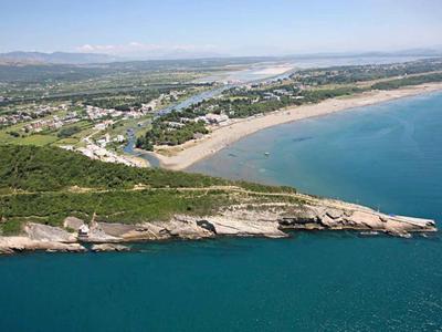 Vue aérienne de la côte avec rochers, plage de sable et un village en arrière-plan.