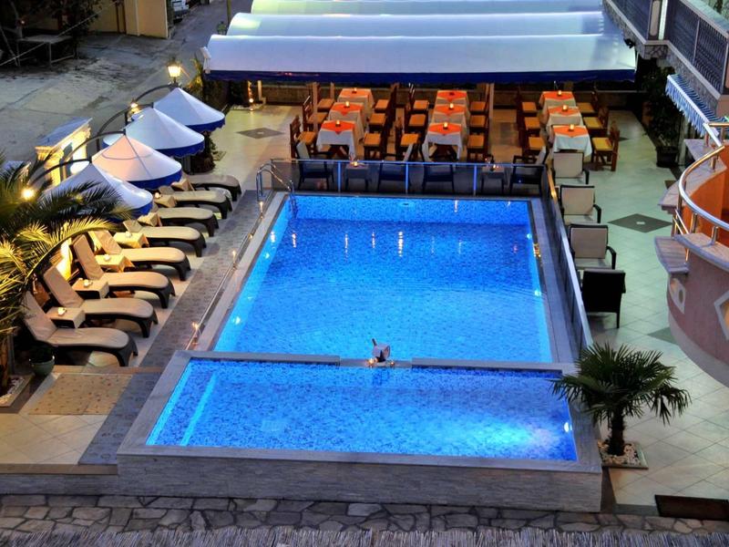 Piscine d'hôtel éclairée avec chaises longues et espace repas la nuit.