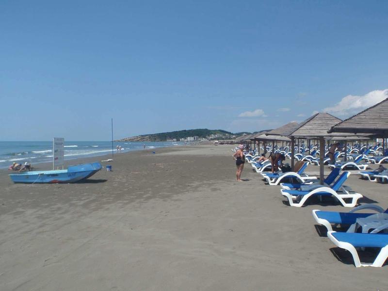 Large plage de sable avec chaises longues et parasols près de la mer calme sous un ciel bleu.