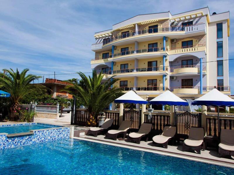 Piscine d'hôtel moderne avec chaises longues, parasols et bâtiment à plusieurs étages en arrière-plan.