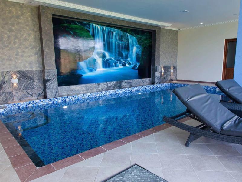 Piscine intérieure moderne avec eau bleue et chaises longues grises à côté du bassin.