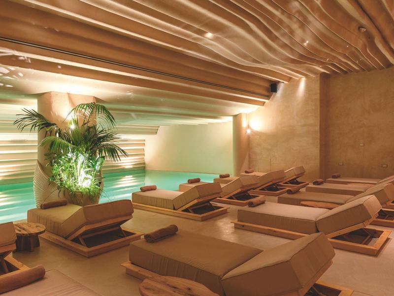 Modernes Spa mit Holzbänken, warmem Licht, Pflanzen und wellenförmiger Decke.