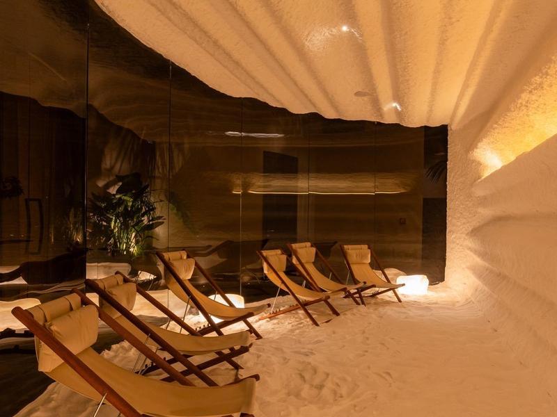 Gemütliche Lounge mit Holzstühlen auf weichem, weißem Sand unter warmem Licht.