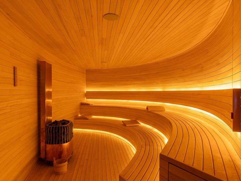 Moderne Sauna mit gewölbter Decke, Holzplanken und indirekter Beleuchtung.