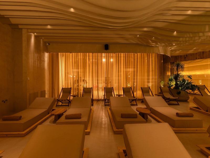 Entspannungsraum mit Liegen, warmem Licht und Vorhängen, ruhige Atmosphäre, moderne Gestaltung.