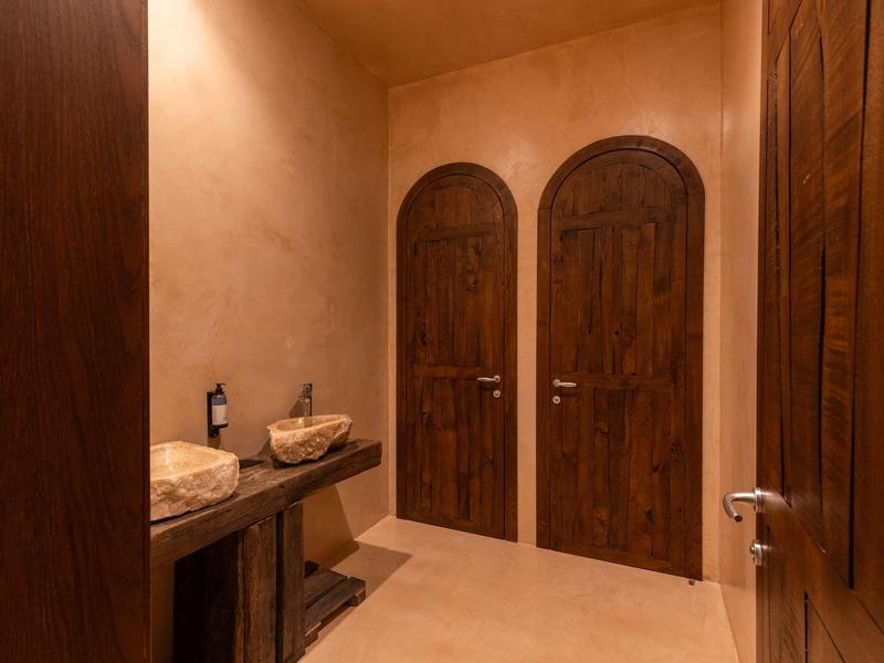 Kleiner Flur mit zwei braunen Holztüren, warmem Licht und rustikalem Holzmöbel mit zwei Waschbecken.
