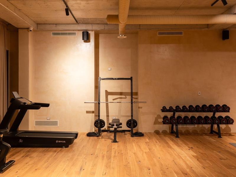 Kleiner Fitnessraum mit Holzfußboden, beige Wänden, Laufband, Hantelbank und Hanteln.