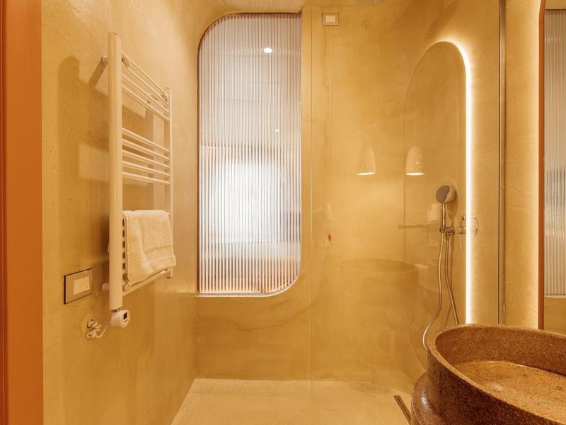 Modernes Badezimmer mit großer Dusche, warmem Licht, abgerundeten Formen und braunem Steinwaschbecken.