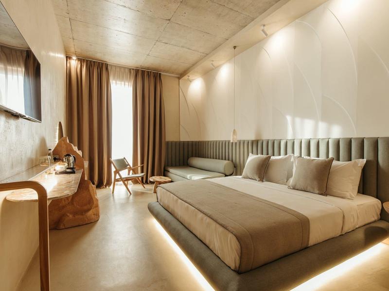 Modernes Schlafzimmer mit großem, beige Bett, grauem Sofa, Holzdecke und Vorhängen.