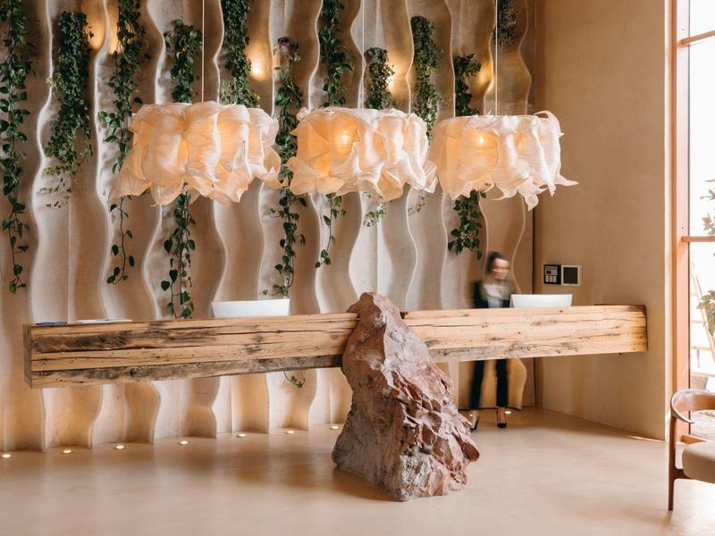 Moderner Tisch aus Holz mit organischer Skulptur als Beine, davor Hängelampen und grüne Wanddeko.