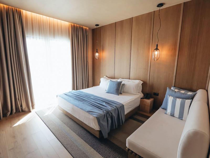 Gemütliches Schlafzimmer mit Holzwänden, großem Fenster, hellem Bett und blau-weißem Dekor.