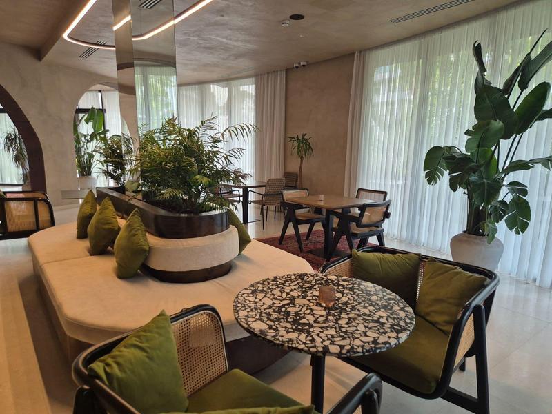 Modernes Wohnzimmer mit Sofa, grünem Kissen, Pflanzen und Marmor-Couchtisch vor großen Fenstern.