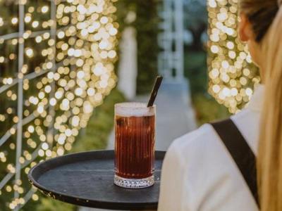 Osoba drží tác s nápojem před osvětlenou venkovní plochou