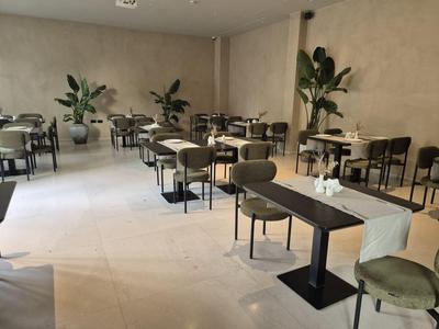 Moderní prázdná restaurace s stoly, židlemi a rostlinami podél zdí.