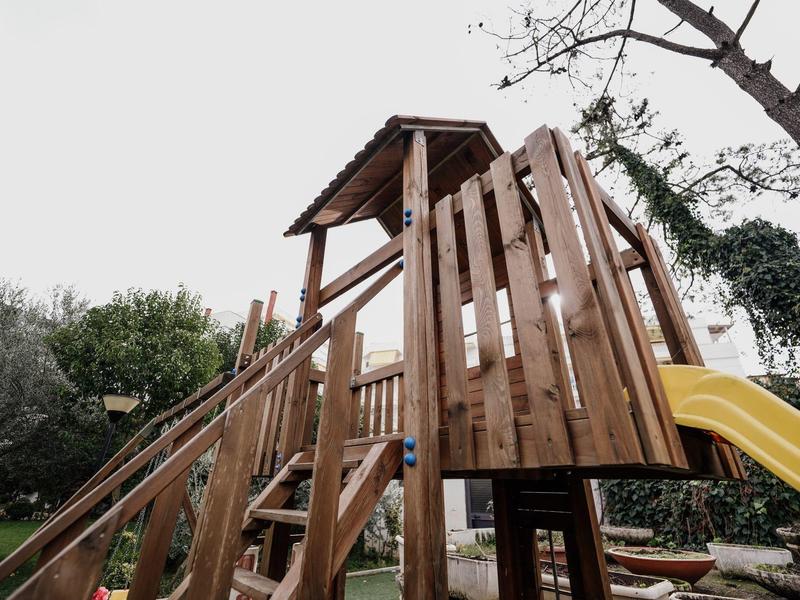 Holz-Klettergerüst mit Rutsche und Treppe in einem Garten mit Bäumen und Gras.
