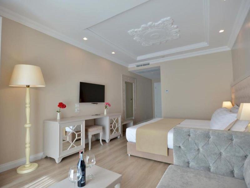 Modern eingerichtetes Schlafzimmer mit hellen Wänden, Fernseher, Bett und stehender Lampe.