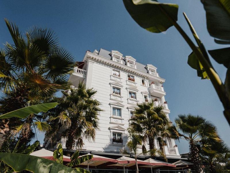 Mehrstöckiges weißes Gebäude mit Palmen und blauem Pool vor klarem Himmel.