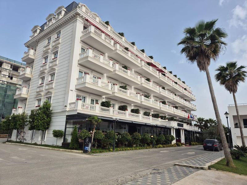 Großes weißes Gebäude mit Balkonen an jeder Etage, umgeben von Palmen und Gehwegen.