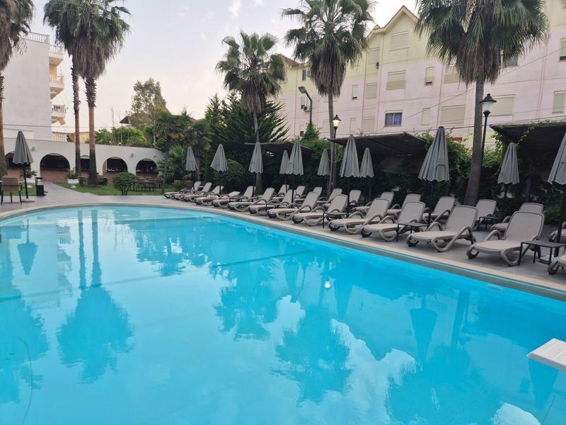 Großer Pool mit klar blauem Wasser, umgeben von weißen Liegestühlen und Palmen.