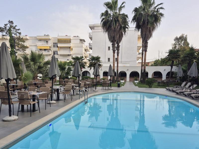 Moderner Swimmingpool mit blauer Wasseroberfläche, Sonnenschirmen, Liegestühlen und Palmen im Hintergrund.