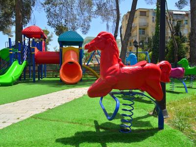 Bunter Spielplatz mit Rutschbahnen und einem roten Federpferd im Gras nahe einem Hotel.