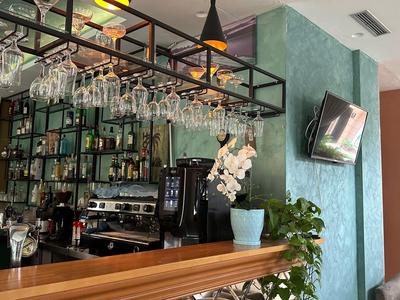 Bar dell'hotel moderno con bancone in legno, bicchieri da vino sospesi e scaffali illuminati pieni di bottiglie.