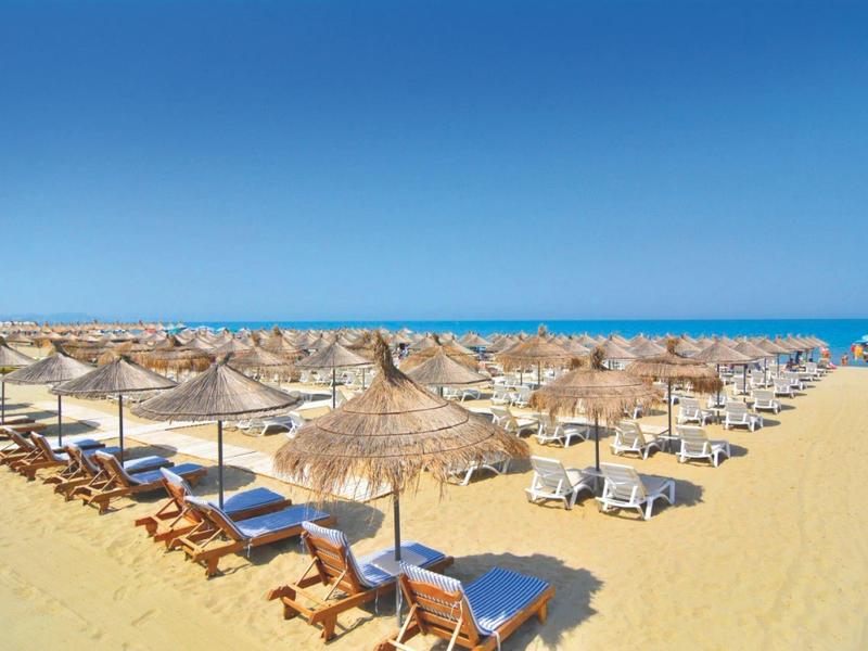 Großer Sandstrand mit zahlreichen Liegen und Strohhut-Sonnenschirmen unter klarem blauem Himmel.
