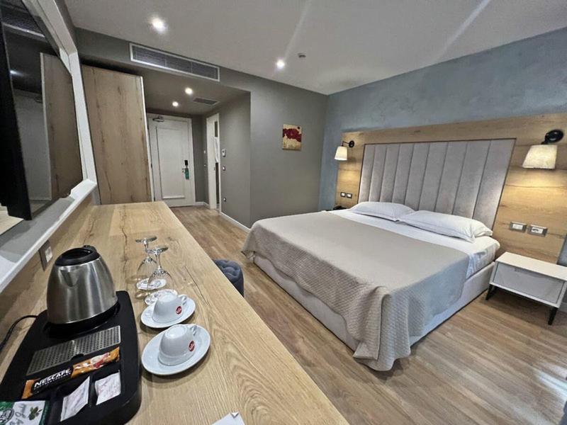Modernes Hotelzimmer mit Doppelbett, Holzboden und Schreibtisch mit Tee- und Kaffeezubehör.