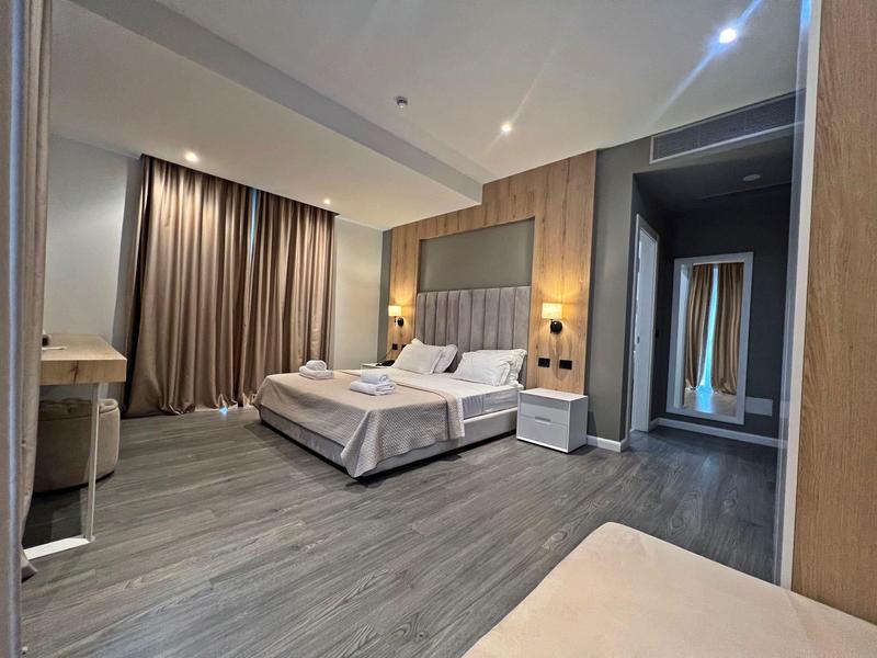 Modernes Hotelzimmer mit Doppelbett, Nachttischen und Holzfußboden in warmen Tönen.