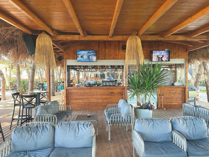 Offene Strandbar mit weichen Sitzgelegenheiten, Holzdach und TVs über der Bar.