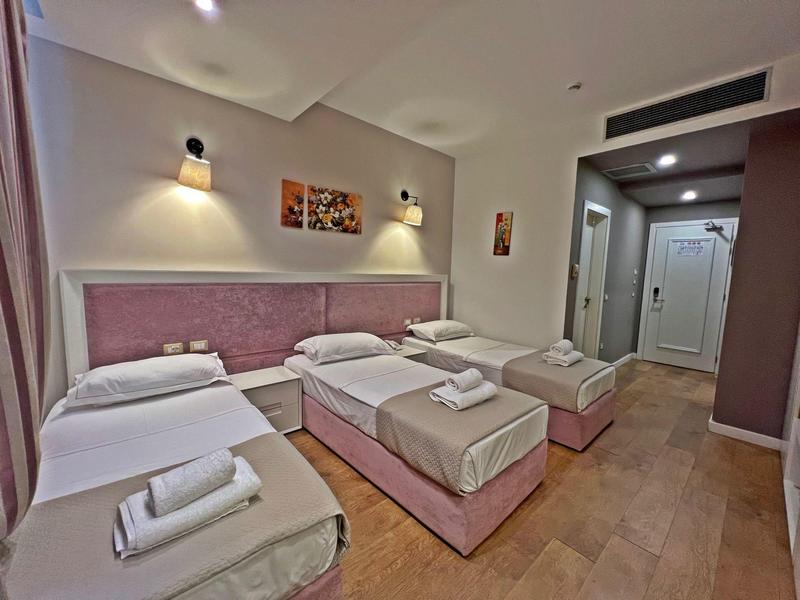 Hotelzimmer mit vier Einzelbetten, weißen Bettlaken und Handtüchern auf hellbraunem Boden.