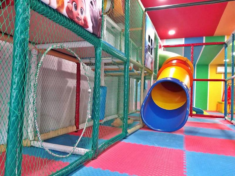 Bunter Indoorspielplatz mit Tunnelrutsche und Netzstrukturen auf gefliesten, weichen Bodenmatten.