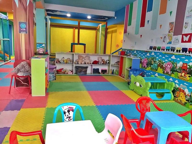 Bunter Spielraum mit weichen Matten, Kindertischen, Stühlen und Spielzeug an den Wänden.