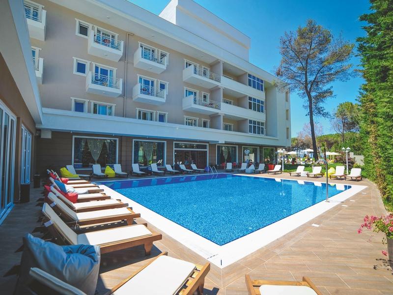 Moderner Außenpool mit Liegestühlen und mehrstöckigem Hotelgebäude im Hintergrund.