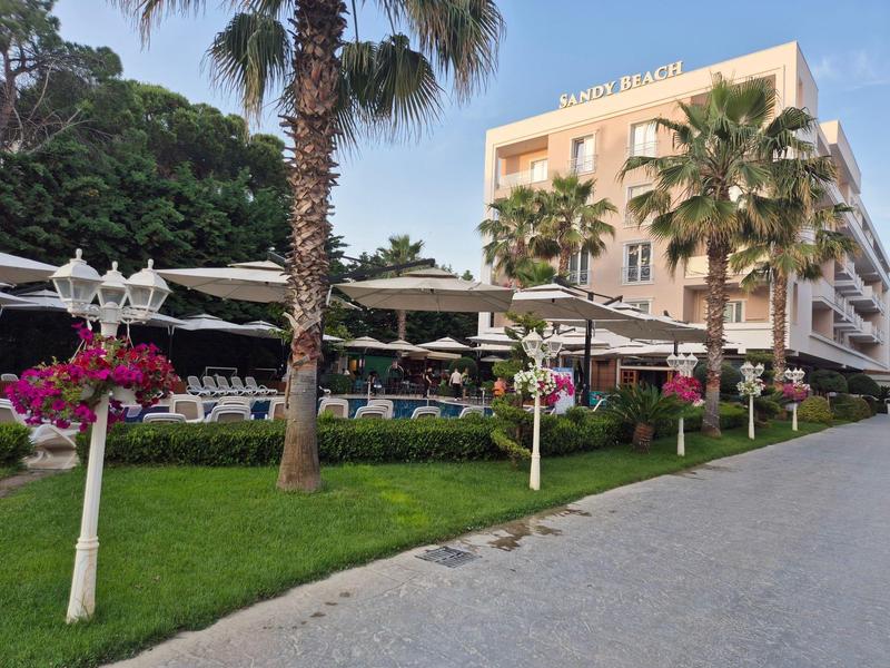 Hotel mit Poolbereich, Sonnenschirmen und Palmen neben einem gepflasterten Gehweg