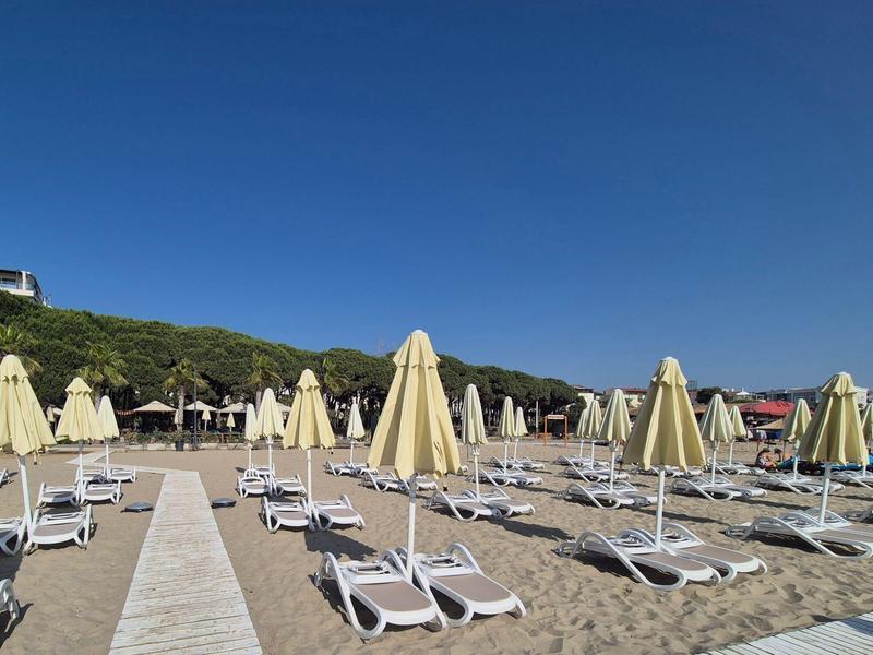Leerer Strand mit Liegen und geschlossenen Sonnenschirmen bei klarem Himmel.