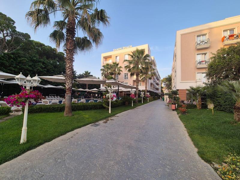 Ein gepflasterter Weg zwischen gepflegten Rasenflächen, Palmen und Gebäuden unter klarem Himmel.